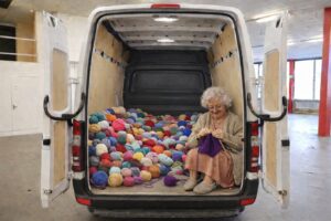 Oma sitzt im Kastenkumpel Transporter und strickt im Laderaum. Es liegt ganz viel Wolle.